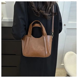 Brown leather bucket bag with dual handles and slim shoulder strap shown on a model