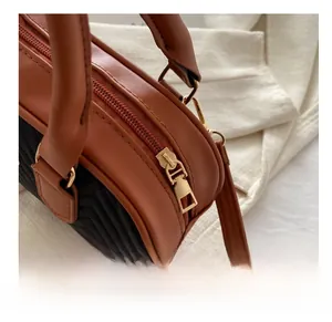 Detail of smooth gold zipper and brown leather handle on a V-quilted crossbody bag