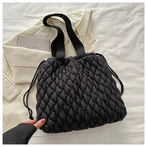 Detail einer gesteppten schwarzen Puffer-Tote-Bag mit Kordelzug auf weichem Stoffhintergrund