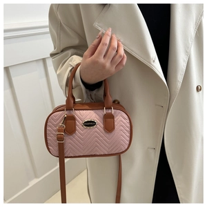 Detail of pink quilted handbag with brown leather handles worn by a model in a beige coat