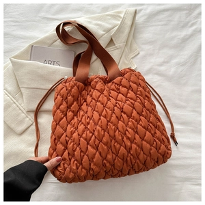 Detailansicht der orangefarbenen Stepptasche mit Kordelzug und braunen Tragegriffen auf Stoff