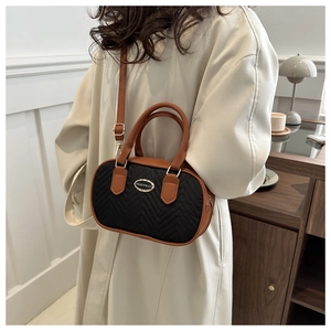 Detail of a mini quilted boston bag with brown leather handles worn with a beige coat