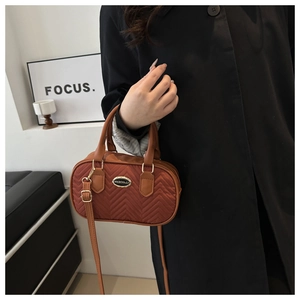 Detail of reddish-brown quilted handbag with herringbone stitching and gold-tone hardware