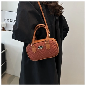 Close-up of brick red quilted Boston bag with leather handles and dual zipper closure