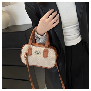 Detail of Boston bag with V-shaped quilting, metal logo, and adjustable brown strap