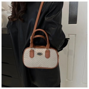 Model wearing a beige quilted crossbody bag with brown leather trim and metal logo plate
