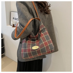 Détail du sac à bandoulière à carreaux rouge et gris avec sangle en cuir et logo