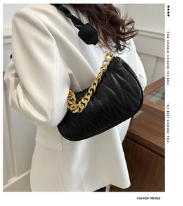 Detail of black pleated leather underarm bag with chunky gold chain and woven strap