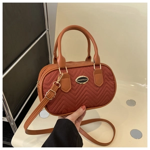 Close-up of V-shaped quilted rust red handbag with gold logo and adjustable shoulder strap