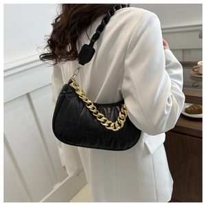 Detail of black quilted leather shoulder bag with gold chain and woven strap in urban setting