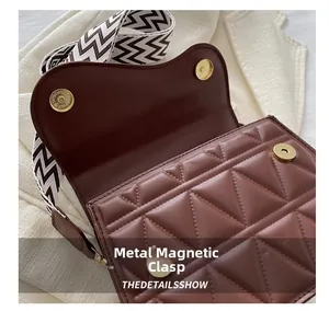 Dettaglio di una borsa a sella marrone con goffratura geometrica e fibbie metalliche dorate