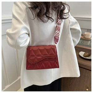 Dettaglio borsa trapuntata rossa con tracolla geometrica su un blazer bianco