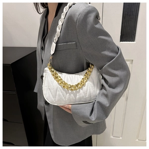 Close-up of white quilted handbag with chunky gold chain strap worn by a model