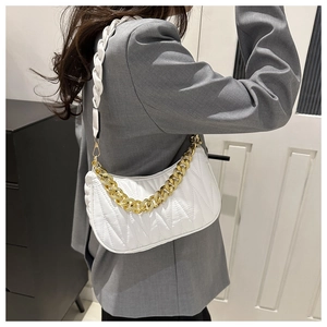 Detail of white quilted hobo bag featuring a gold chain and woven strap over a gray suit
