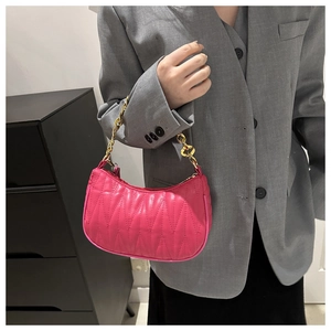 Close-up of hot pink quilted baguette bag with chunky gold chain strap on a model
