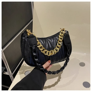 Detail of black quilted baguette bag with glossy pleated finish and gold chain strap