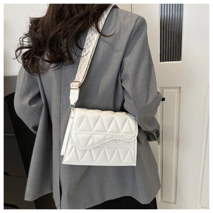 Dettaglio borsa trapuntata bianca con tracolla geometrica larga su blazer grigio