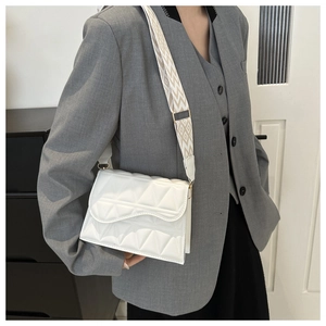 Dettaglio borsa trapuntata bianca con patta ondulata e tracolla larga a motivo geometrico