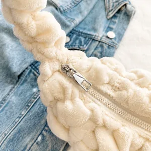 Detail shot of a smooth silver metal zipper on a white plush textured shoulder bag