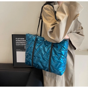 Detail of blue quilted puffer tote bag with metallic finish and black shoulder strap