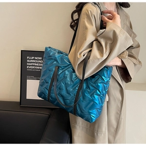 Close-up of bright blue quilted tote bag with metallic gloss and black handles on a model