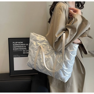 Detail of silver metallic quilted tote bag featuring padded texture and beige shoulder straps