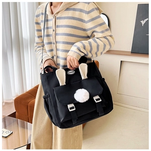 Detail of cute black canvas crossbody bag with white bunny ears and plush ball decoration