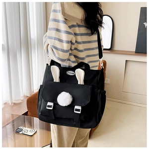 Detail showing plush rabbit ears and pom-pom accent on this black nylon crossbody bag