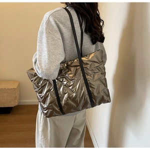 Detailed view of the large metallic bronze quilted tote bag worn by a model in a room