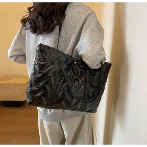 Detail of black quilted puffer tote bag with glossy finish and thin leather straps