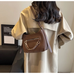 Detail of brown pebbled leather underarm bag featuring a chunky gold chain and zip pocket