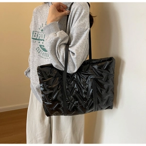 Detail view of black quilted puffer tote bag made of glossy nylon with leather straps