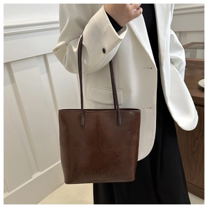 Side view of retro dark brown leather bucket bag on model with minimalist white suit