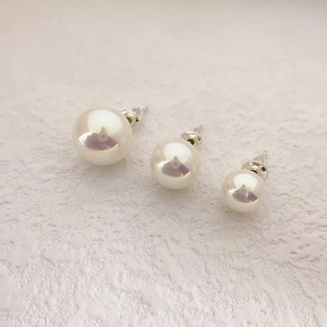 Detailed view of three sizes of round glossy pearl earrings on a textured white surface