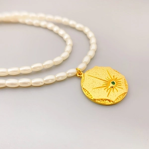 Macro detail of seed pearl necklace with 18K gold plated octagon pendant and green gemstone