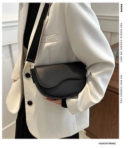 Close-up of black saddle bag featuring matte leather texture and wide woven shoulder strap