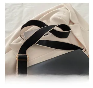 Detail of wide black fabric strap with contrast edges and gold hardware on PU handbag