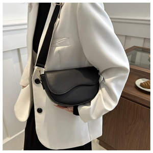 Black saddle bag with wide nylon strap shown on a woman in a white blazer