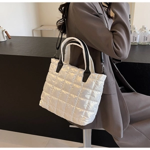 Close-up of white quilted bucket bag with black handles on a brown blazer outfit