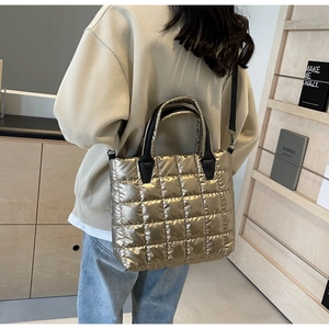Detailed view of a gold puffer handbag with quilted texture and black top handles