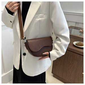 Brown matte PU leather saddle bag with wide canvas strap shown on a model in white blazer