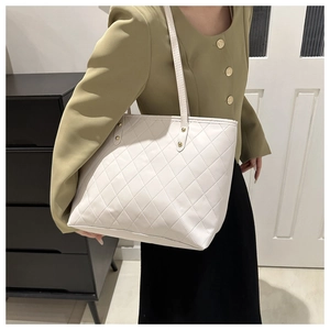 Detail view of cream quilted tote bag featuring gold hardware and shoulder strap