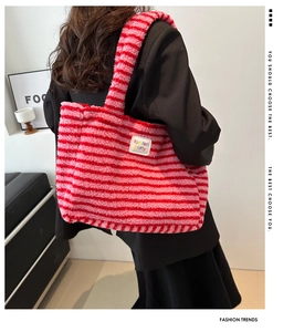 Détail du sac cabas rayé en peluche rouge et rose porté par un mannequin à l'épaule