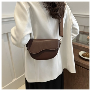 Detail of a dark brown saddle bag featuring a stylish wide woven canvas shoulder strap