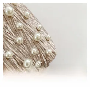 Detailed view of champagne gold pleated fabric adorned with elegant white faux pearls