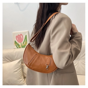 Detail of a brown crescent-shaped patent leather shoulder bag with smooth texture
