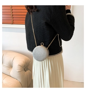 Détail d'un sac de soirée rond argenté brillant avec bandoulière chaîne sur tenue noire