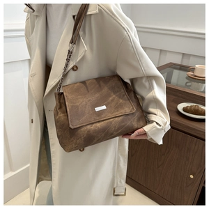 Detail of a brown pleated leather tote bag with silver logo and metal chain strap on table