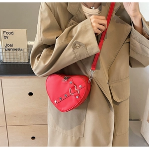 Sac bandoulière rouge en forme de cœur avec clous argentés sur un trench-coat beige