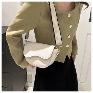 Close-up of a white saddle bag with wide fabric strap and golden hardware on model